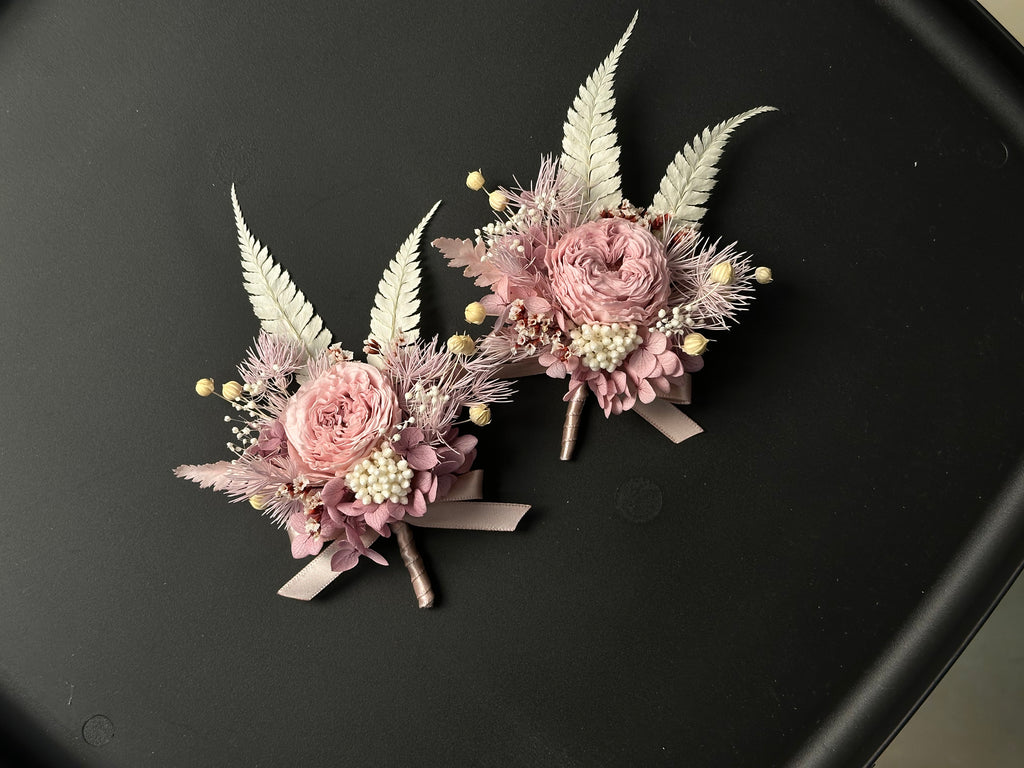 Two dusty pink preserved flower brooches with pale fern leaves and ribbon, shown together; sold individually.