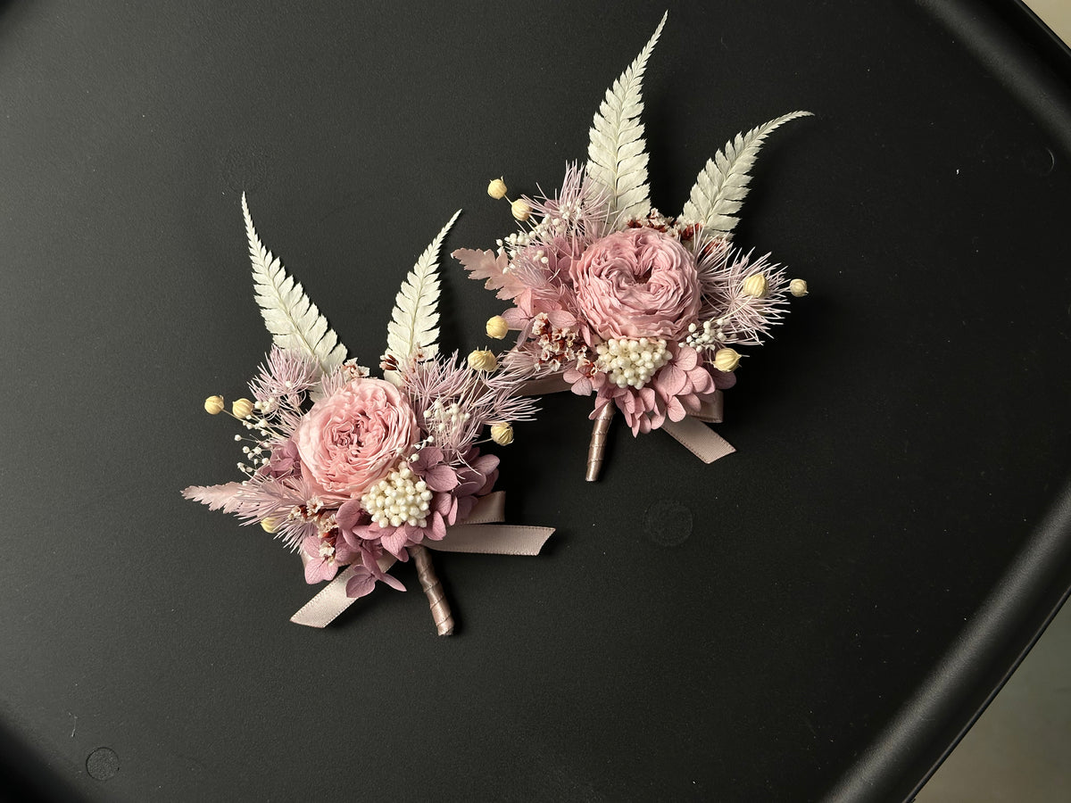 Two dusty pink preserved flower brooches with pale fern leaves and ribbon, shown together; sold individually.