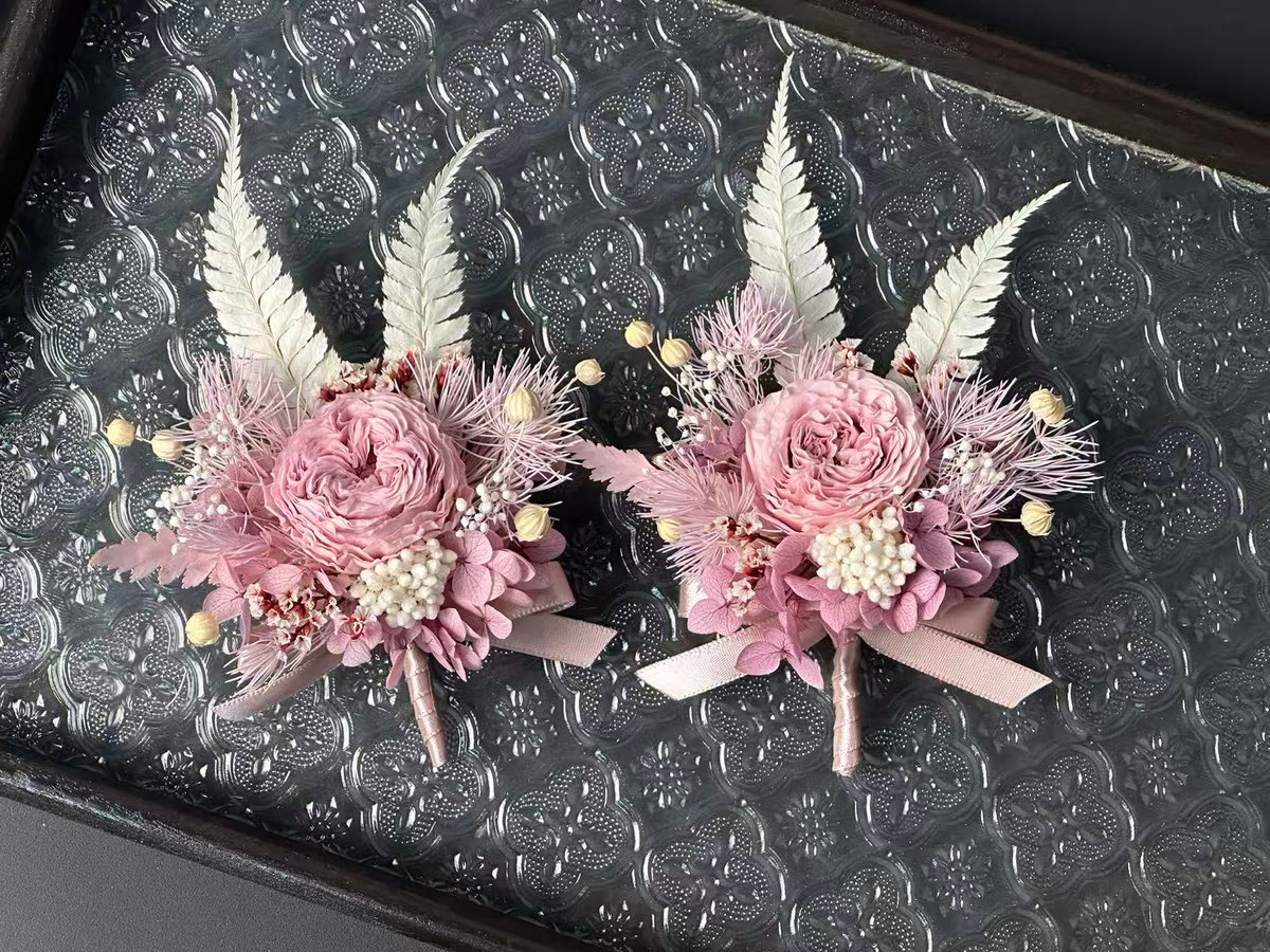 Two dusty pink preserved flower brooches on a patterned glass tray, upright with stems pointing down; sold individually.